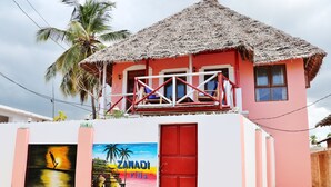 Eine pinkfarbene Villa mit einem Strohdach, einer roten Tür und einem Balkon mit weißem Geländer.