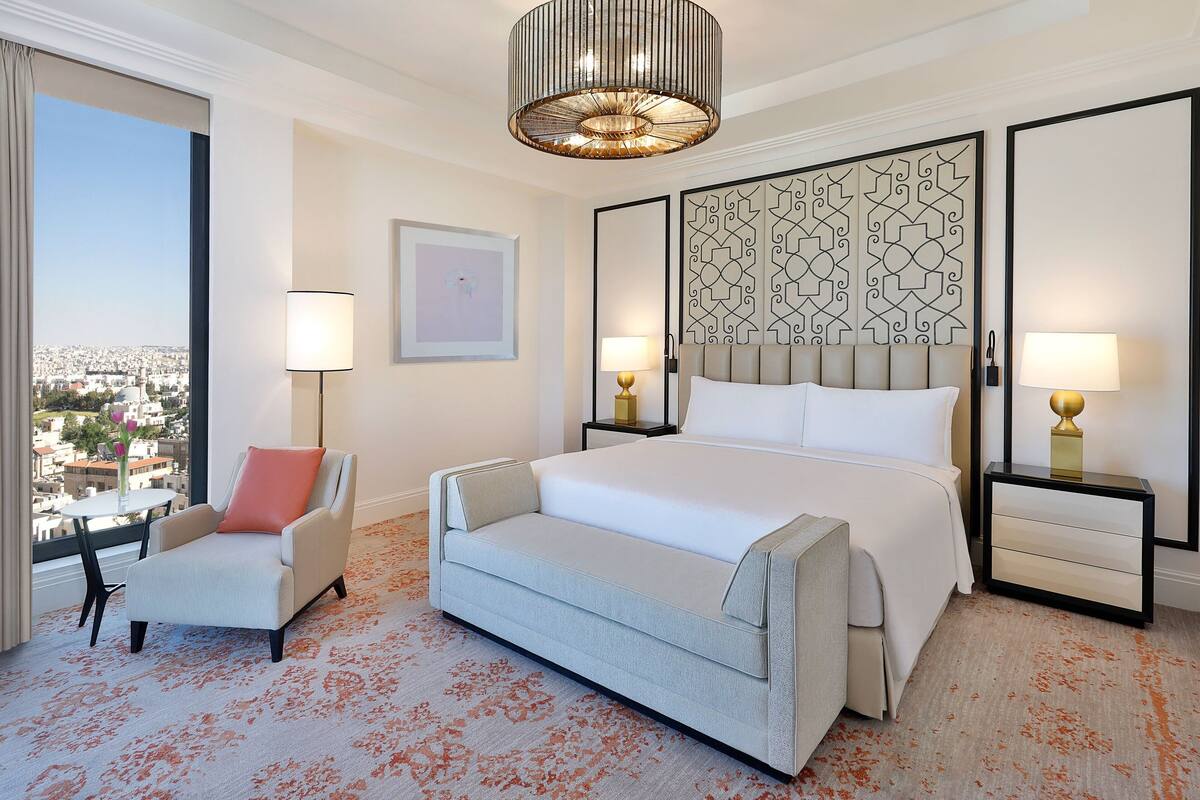 A hotel room with a large bed, a sofa, a nightstand, and a view of the city.