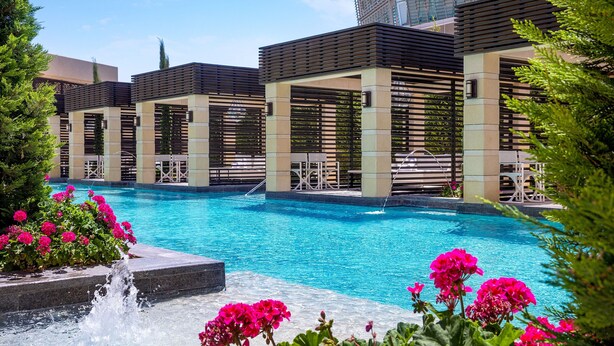 A swimming pool with a modern architectural design, surrounded by lush greenery and vibrant flowers. - The St. Regis Amman (Amman)