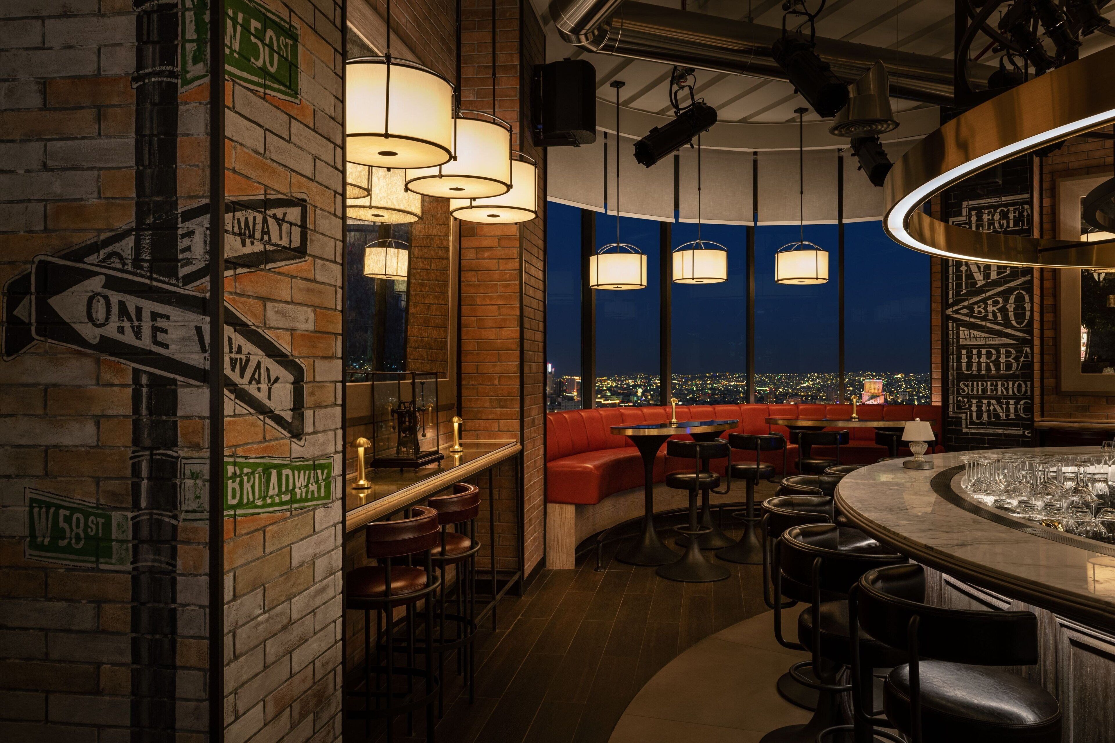 A bar area with a brick wall, directional signs, and a view of the city at night.