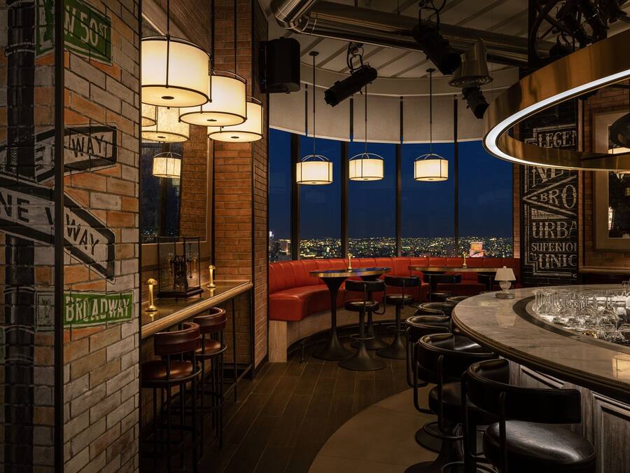 A bar area with a brick wall, directional signs, and a view of the city at night.