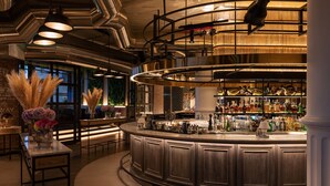A bar area with a curved counter, shelves of bottles, and hanging lights. - The St. Regis Amman (Amman)