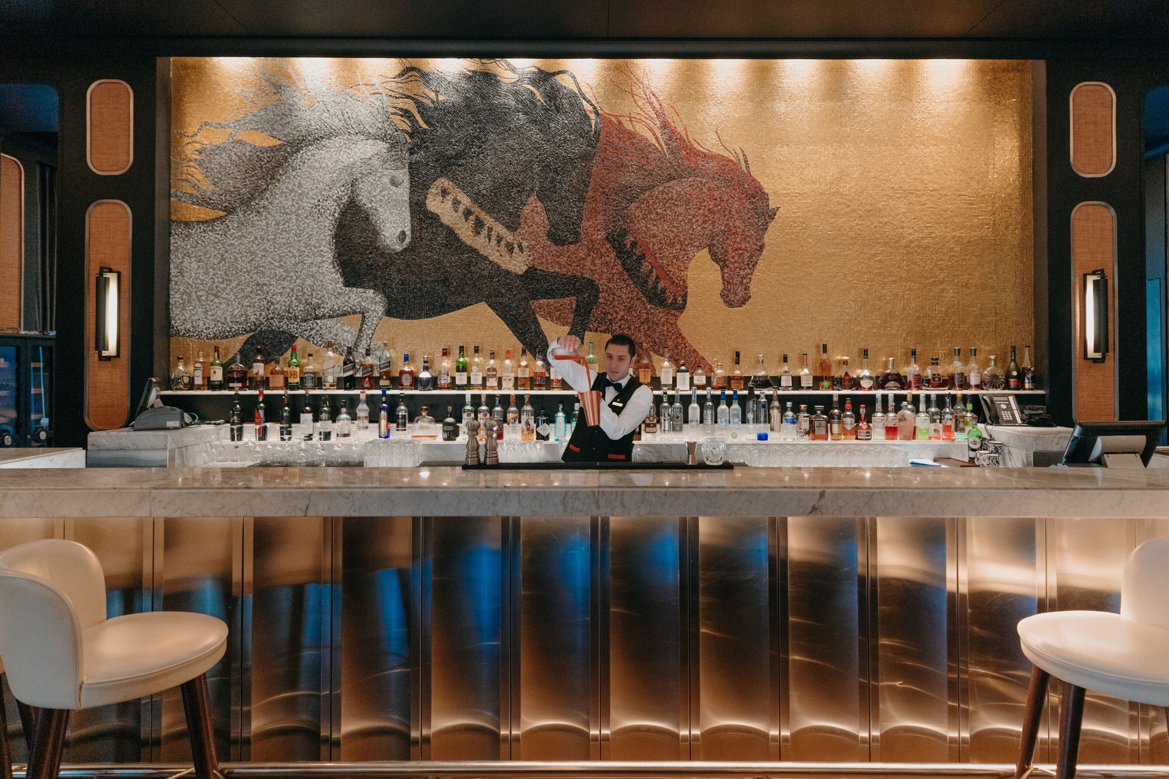 A bar area with a bartender, a large horse mural, and a variety of liquor bottles.
