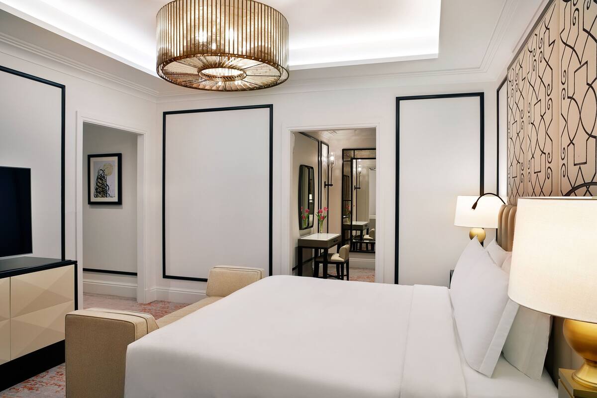 A hotel room with a large bed, a desk, a chair, a television, and a mirror.
