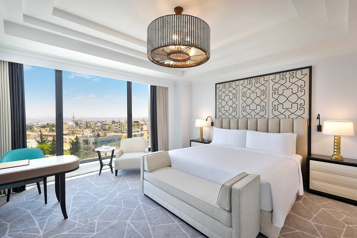 A hotel room with a large bed, a desk, a chair, and a view of the city.
