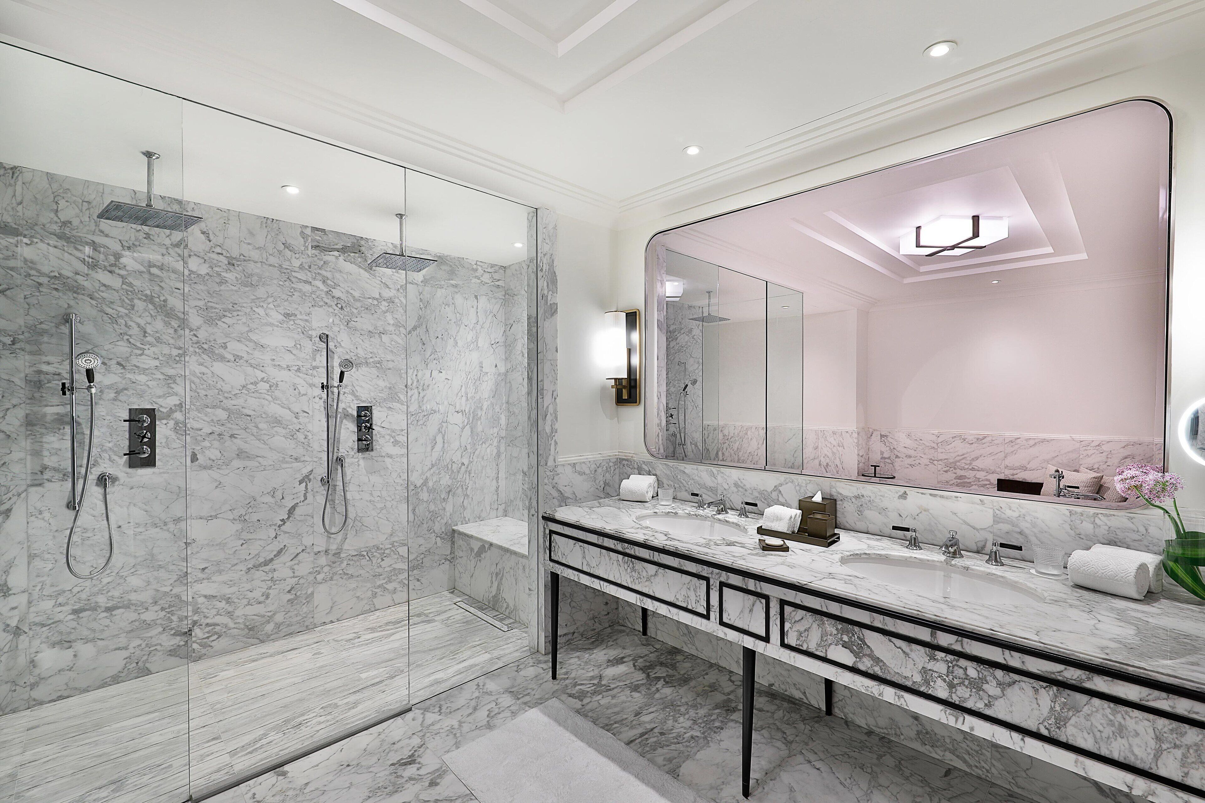 Une salle de bain moderne avec un grand miroir, des murs en marbre, une douche à l’italienne et un meuble-lavabo.