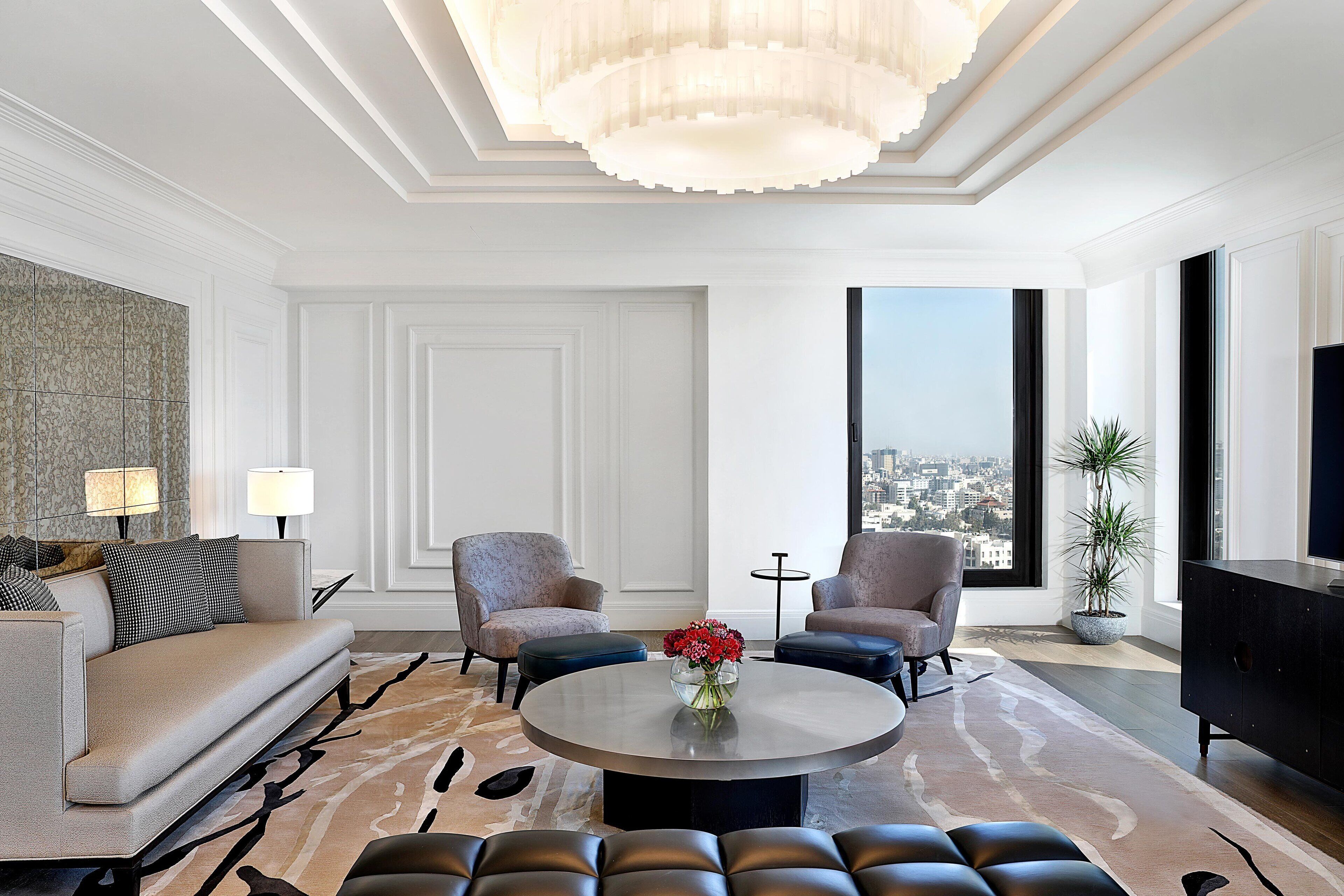 Ein modernes Wohnzimmer mit einer Couch, zwei Sesseln, einem Couchtisch und einem großen Fenster mit Blick auf die Stadt.