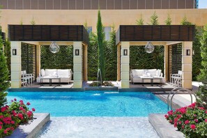 A pool area with two seating areas, each with a sofa and a table, surrounded by a pool and a pergola with hanging lights. - The St. Regis Amman (Amman)