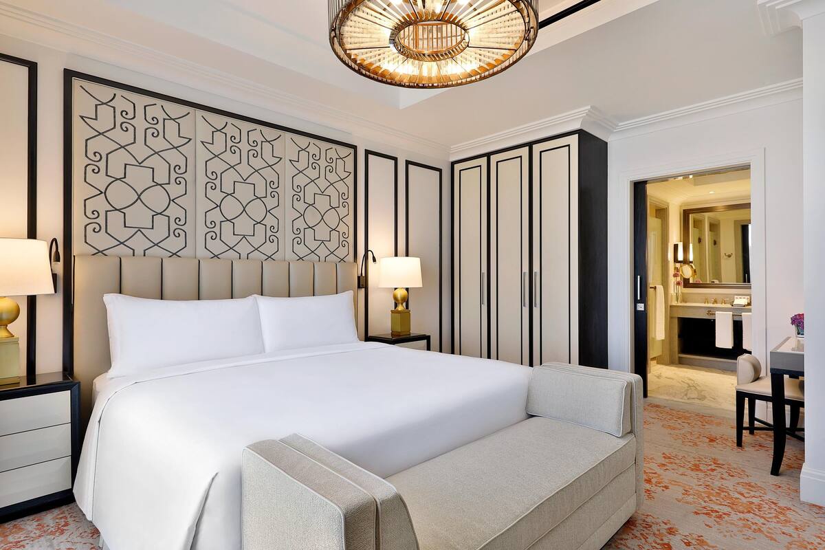 A large bed with a headboard, two bedside tables with lamps, a decorative wall panel, and a bathroom visible through an open door.
