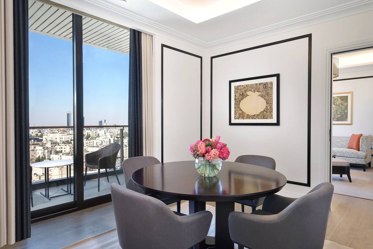 A modern room with a round table, chairs, a vase of flowers, and a city view through large windows.