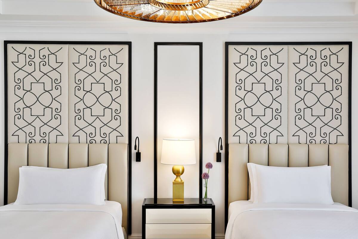 A hotel room with two beds, a nightstand with a lamp, and decorative wall panels.