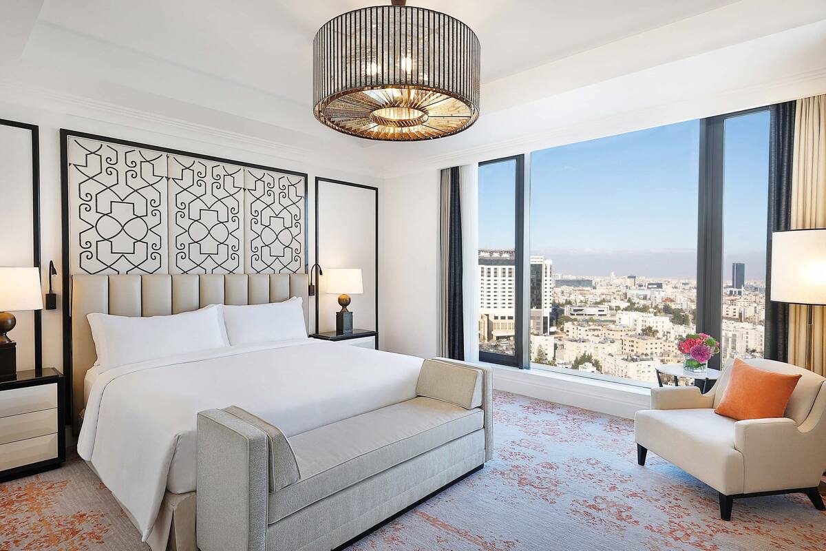 A modern hotel room with a large bed, a sofa, a view of the city, and a decorative headboard.