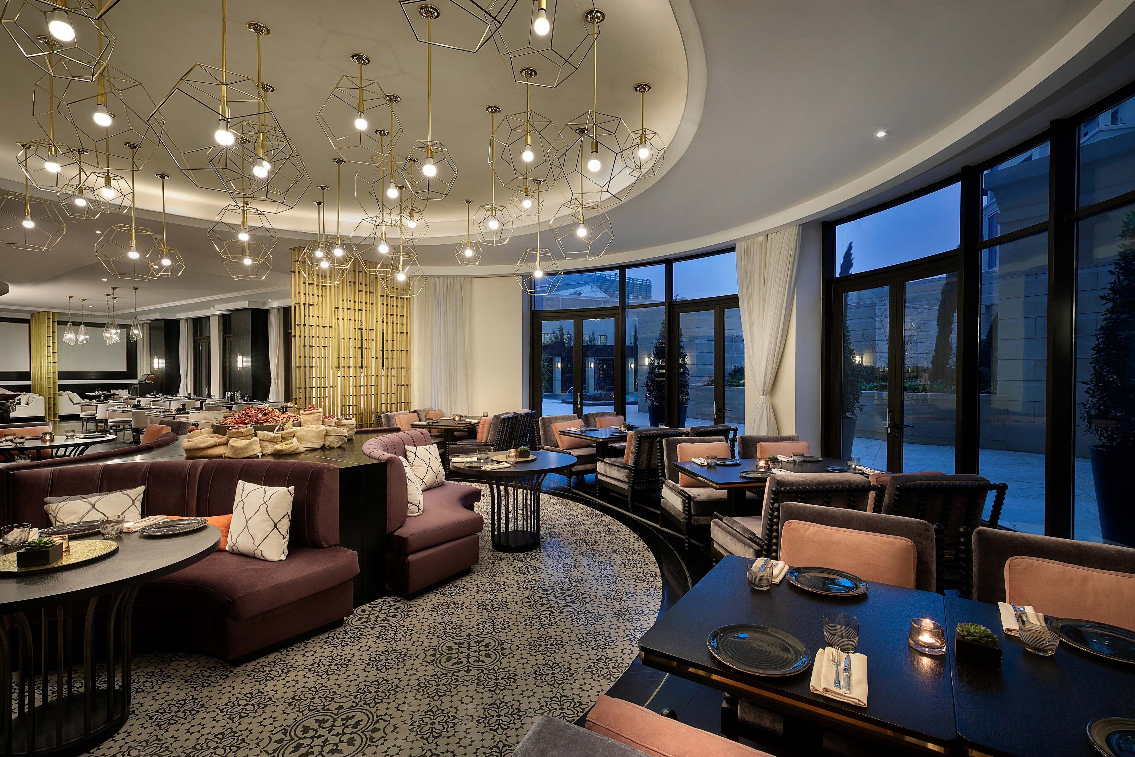 Un moderno vestíbulo de hotel con una zona de estar curvilínea, un comedor y grandes ventanales con vistas a la ciudad.