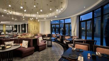 Un moderno vestíbulo de hotel con una zona de estar curvilínea, un comedor y grandes ventanales con vistas a la ciudad.