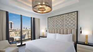 A hotel room with a large bed, a view of the city, a chandelier, and a decorative wall panel. - The St. Regis Amman (Amman)