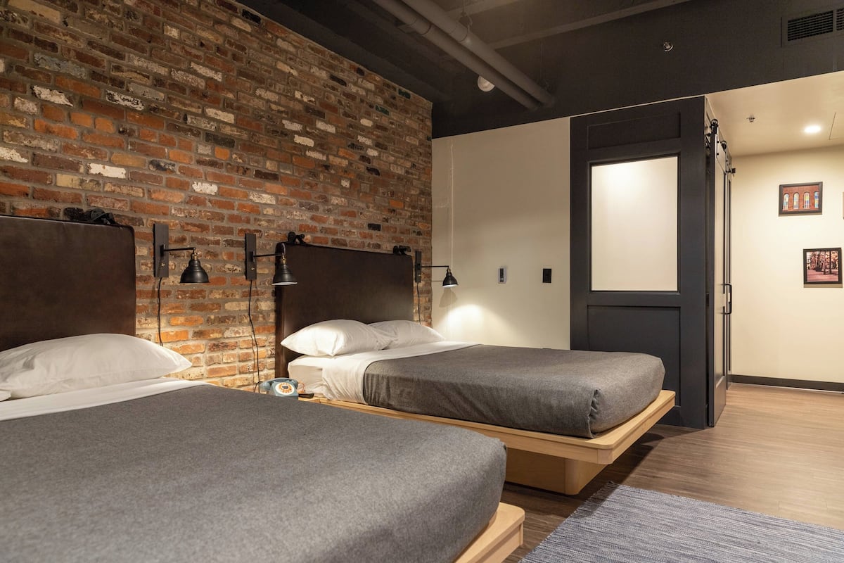 A hotel room with two beds, a brick wall, and a door leading to another room.