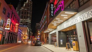 Un hotel chiamato 'Hotel Max' con un neon, adiacente a un negozio di dischi.