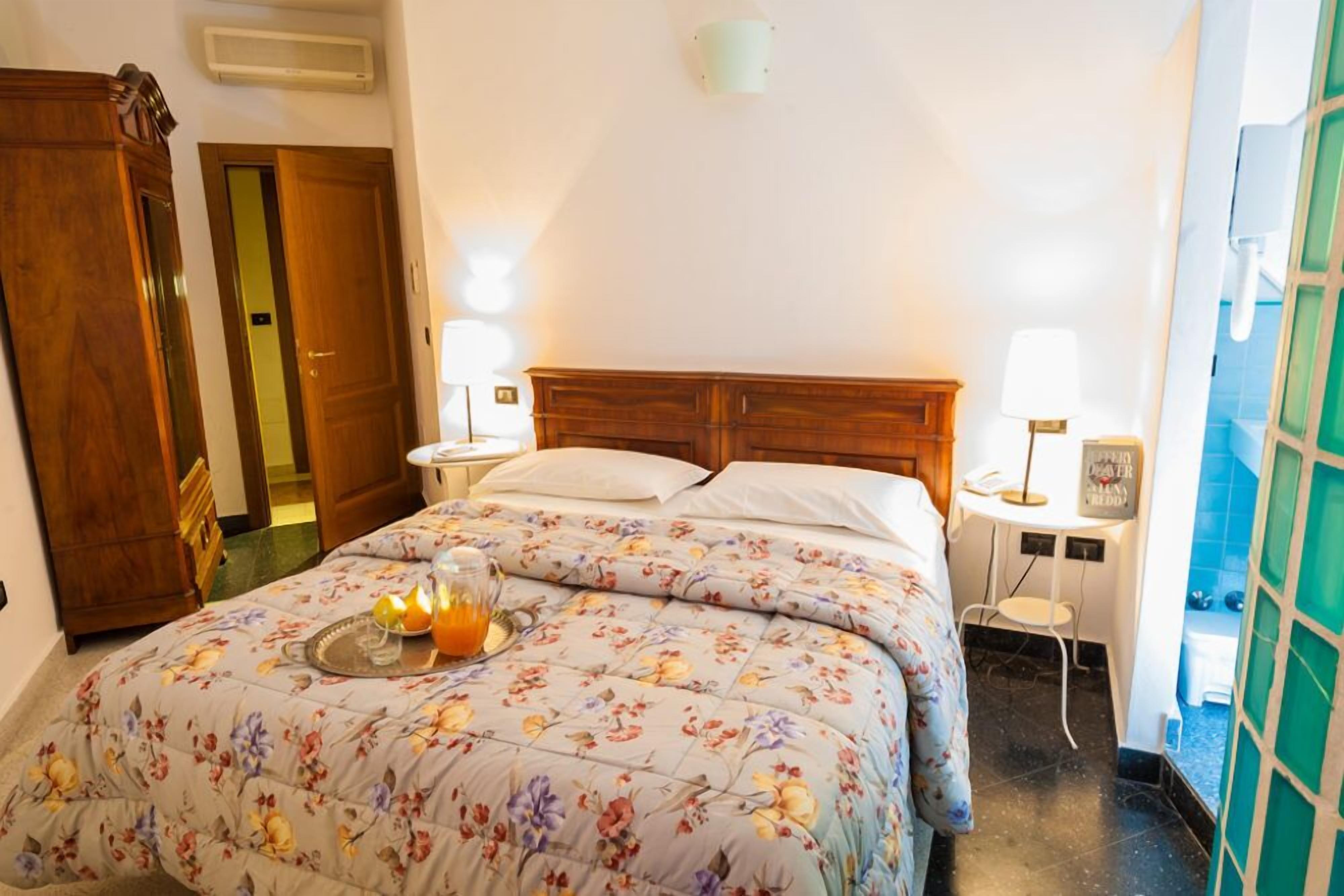 Habitación de hotel con cama, mesitas de noche, armario de madera y baño visible a través de una puerta abierta.