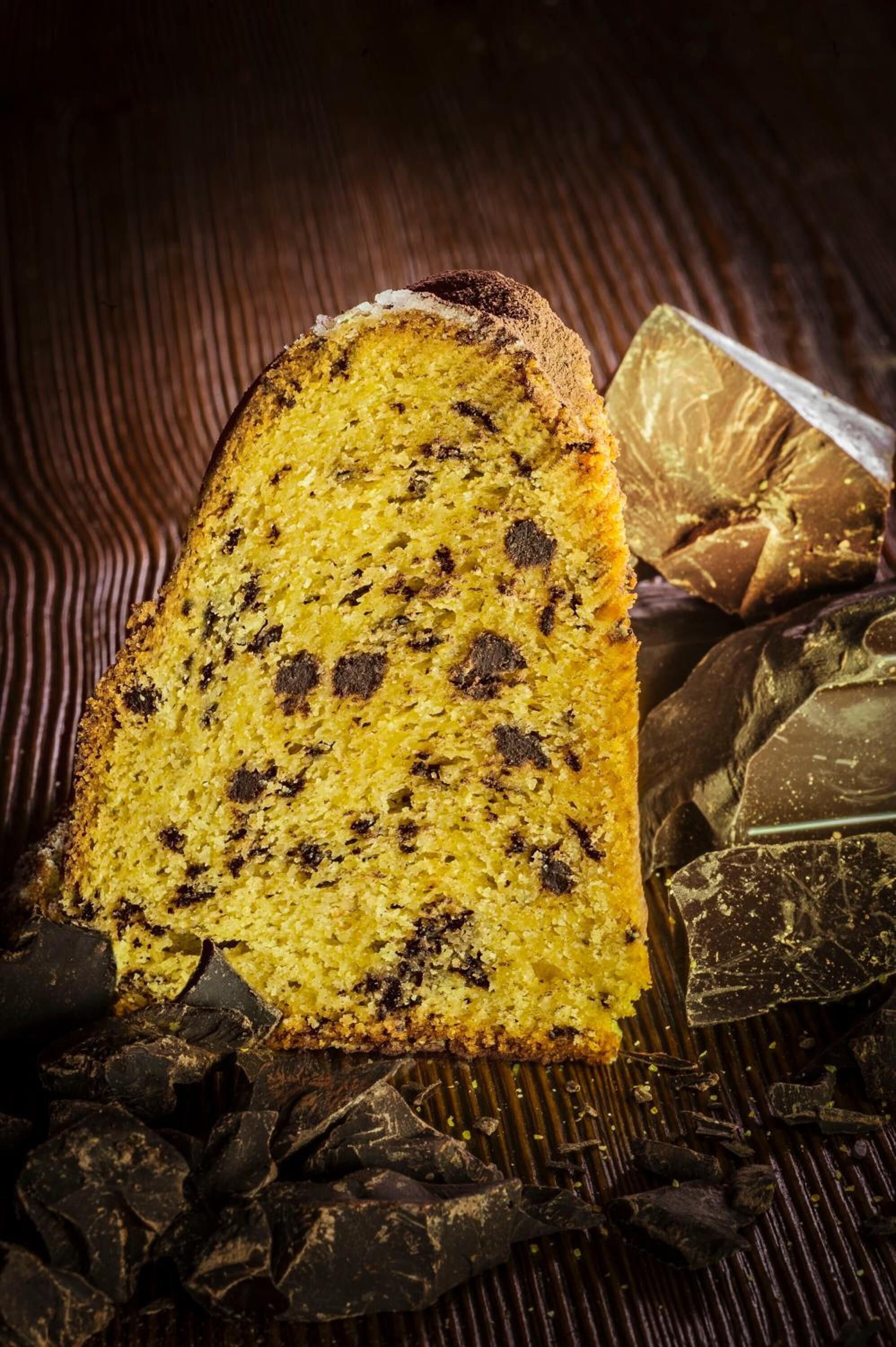 A slice of cake with chocolate chips on a wooden surface.