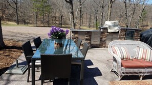 An outdoor patio with a glass-top table, wicker chairs, a wicker sofa with striped cushions, and a stone fireplace. - Hemlock Hide-A-Way Cozy Romantic Private Lake Cabin (Rice Lake)