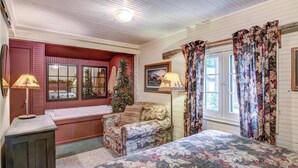 A cozy room with a bed, a chair, a window with curtains, a lamp, and a wall-mounted picture.