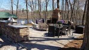 An outdoor patio with stone walls, a stone fireplace, wicker furniture, and a view of a lake. - Hemlock Hide-A-Way Cozy Romantic Private Lake Cabin (Rice Lake)