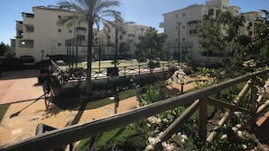 A courtyard with a palm tree, a tennis court, and a building with multiple balconies. - Residencial Duquesa 2239 Sea & Sun (Manilva)