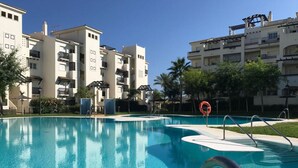 A swimming pool with a clear blue water surface, surrounded by modern buildings with balconies and a clear sky. - Residencial Duquesa 2239 Sea & Sun (Manilva)