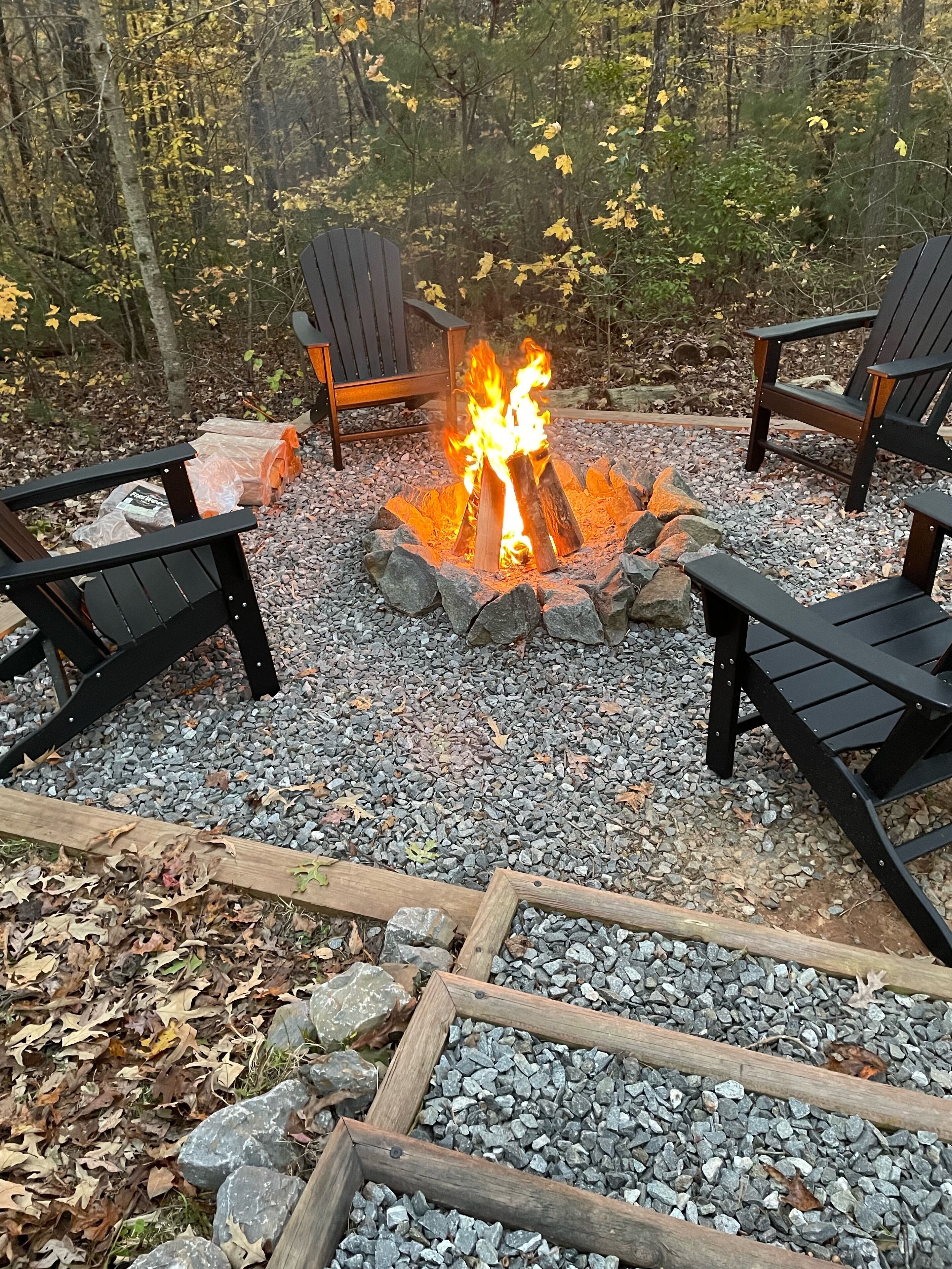 Un foyer avec des bûches, entouré de pierres, et des fauteuils Adirondack disposés autour.