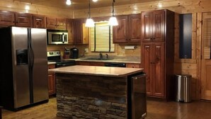Une cuisine dotée de meubles en bois, d’un îlot central en pierre, d’appareils électroménagers en acier inoxydable et de luminaires suspendus.
