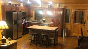 L’intérieur chaleureux d’un chalet, avec un revêtement en bois, un coin cuisine équipé d’un réfrigérateur, d’une cuisinière et de tabourets de bar, ainsi qu’un espace de vie comprenant un canapé et une table basse.