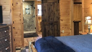 Une chambre dans une cabane en bois, avec un lit, une commode et une grande porte en bois.