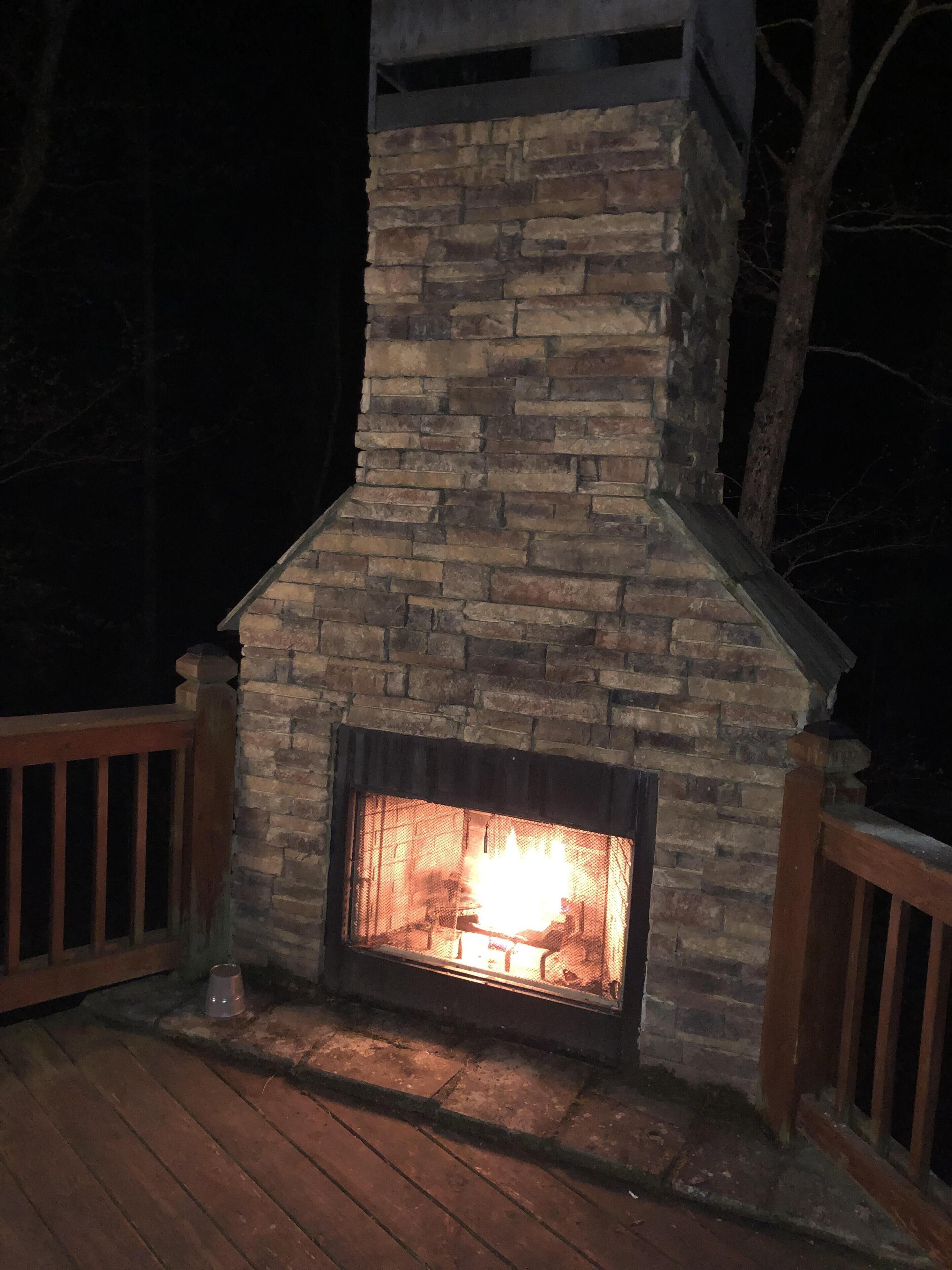 Ein Steinkamin mit Feuer, umgeben von einer Holzterrasse und Geländern.
