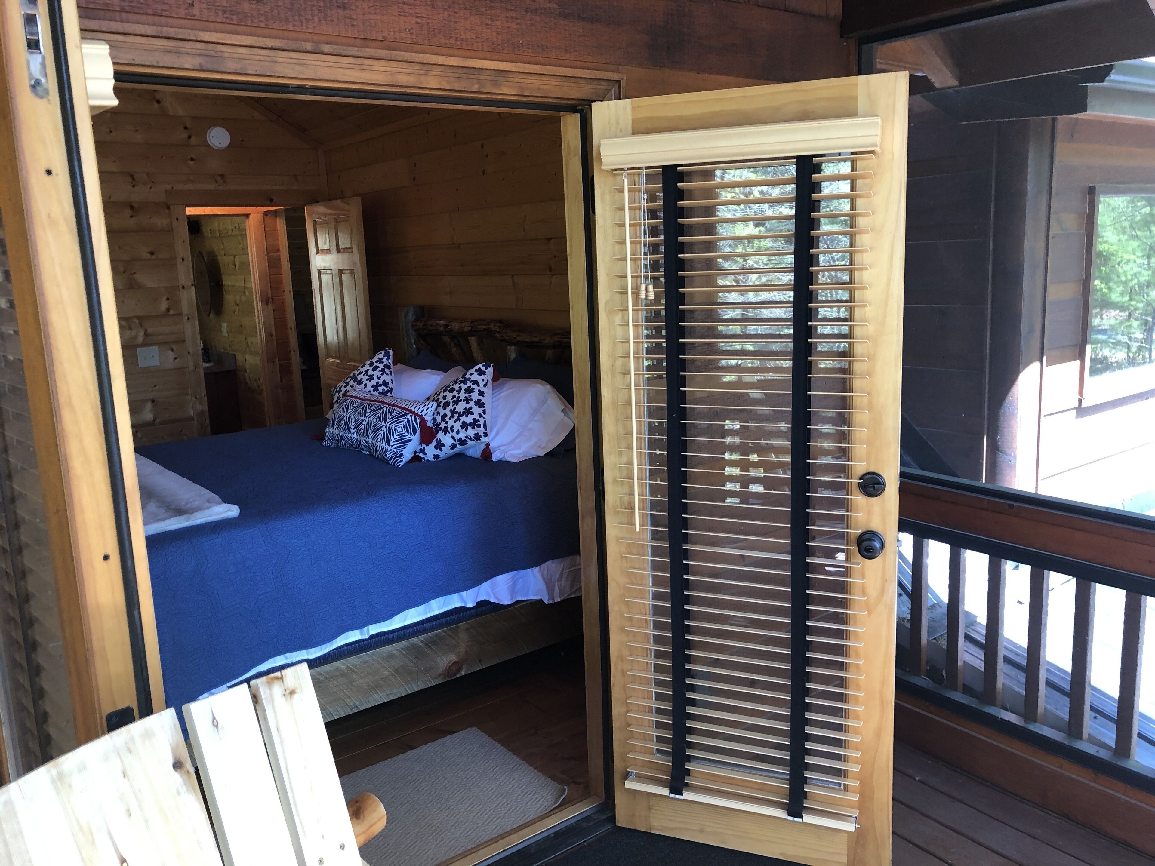Un dormitorio tipo cabaña de madera, con una cama, almohadas y una ventana con persianas.