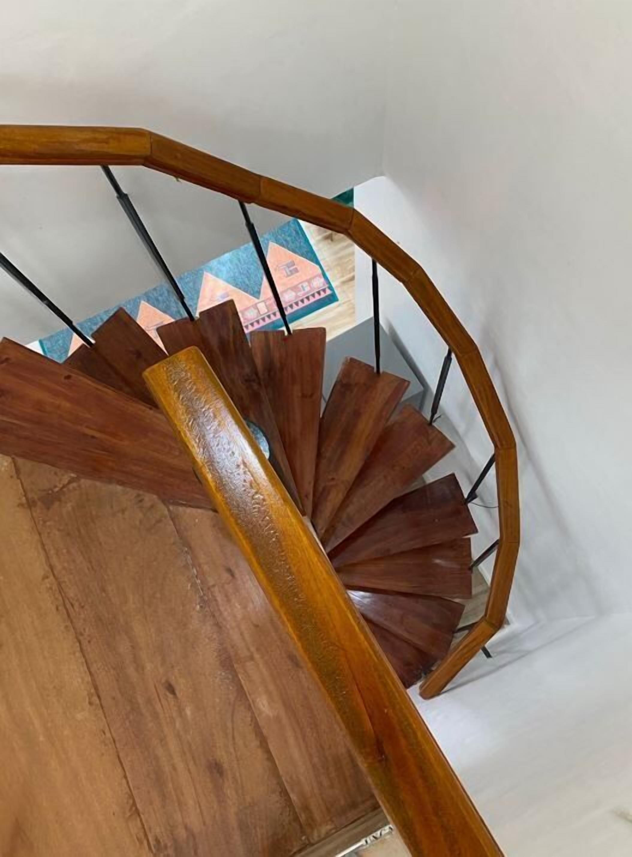 A wooden spiral staircase with a handrail and a view of a room with a geometric-patterned wall.