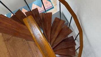 A wooden spiral staircase with a handrail and a view of a room with a geometric-patterned wall.