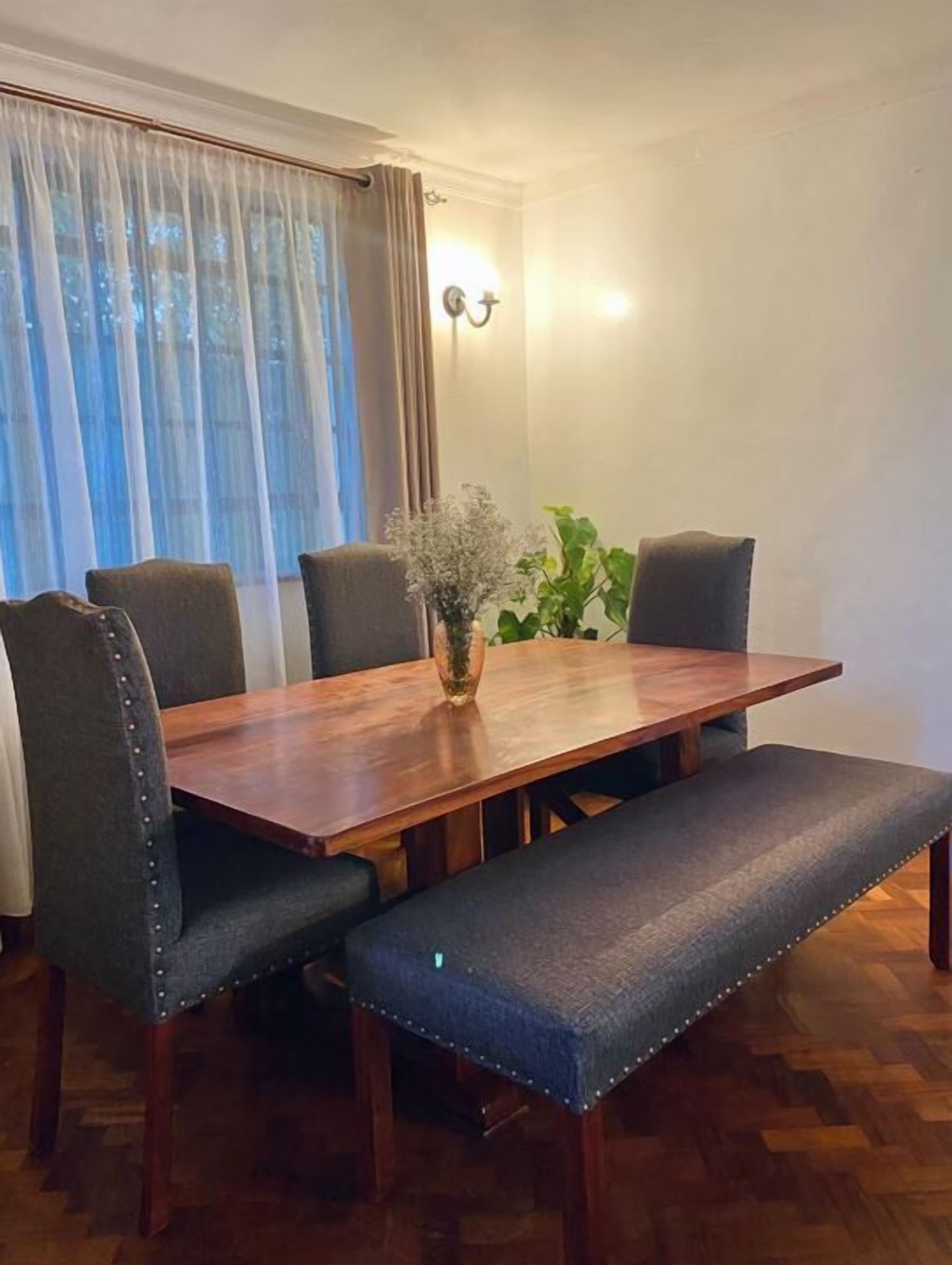 A dining area with a wooden table, four upholstered chairs, a bench, and a vase with flowers.
