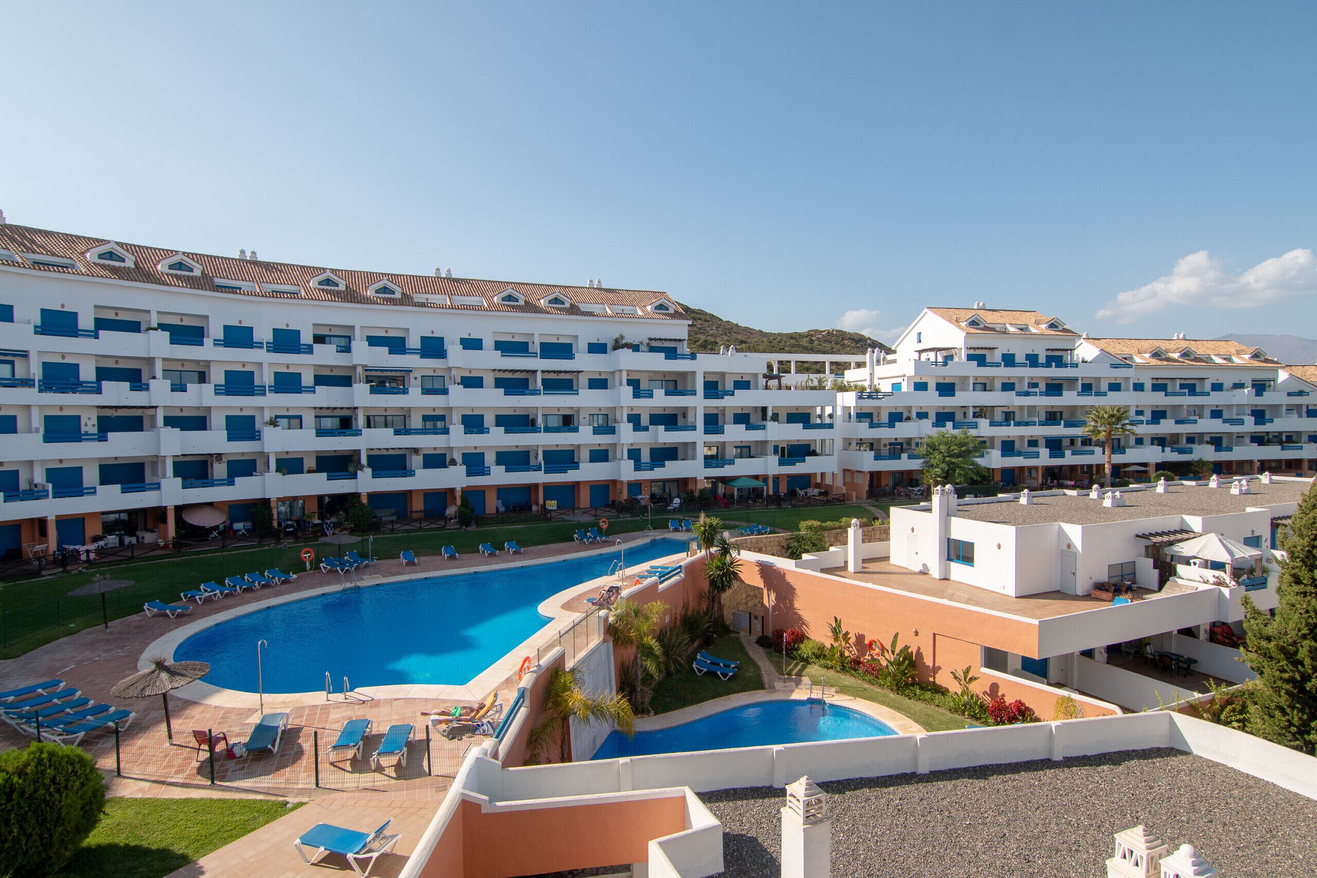 Un hotel con múltiples balcones, una piscina central y un jardín paisajístico.
