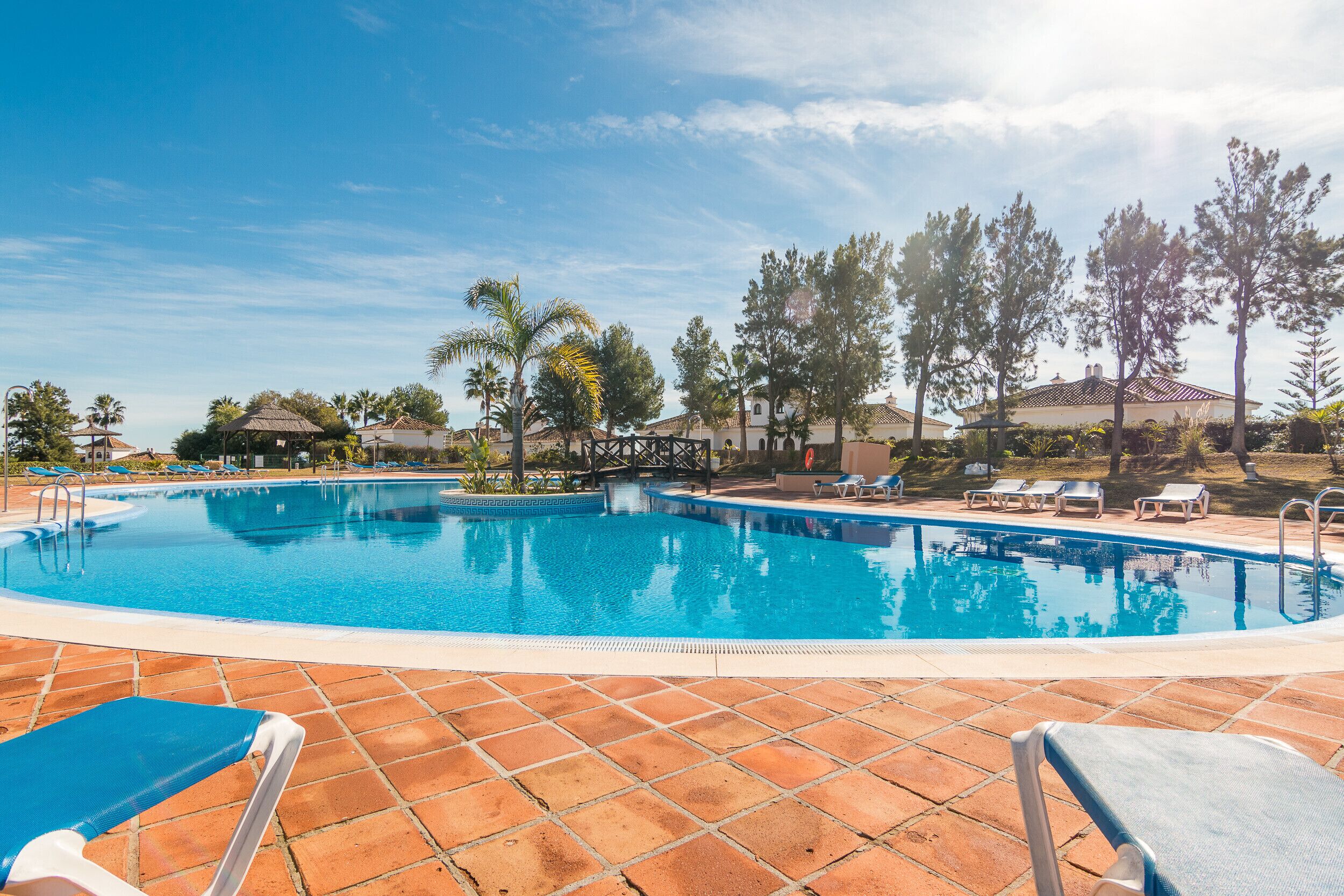 A swimming pool with tiled deck and lounge chairs, surrounded by trees and buildings.