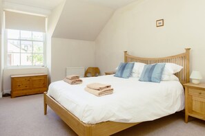 A bedroom with a wooden bed, white bedding, a wooden nightstand, a bedside table, a window, and a radiator.