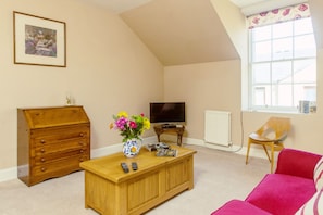 A living room with a wooden cabinet, a coffee table with a vase of flowers, a television, and a red chair.