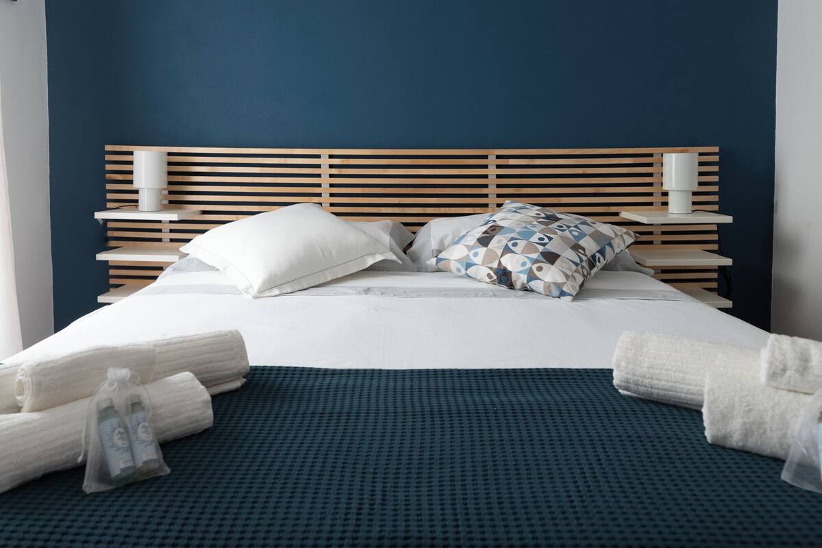 Una cama bien hecha con colcha azul, dos almohadas y cabecera de madera.
