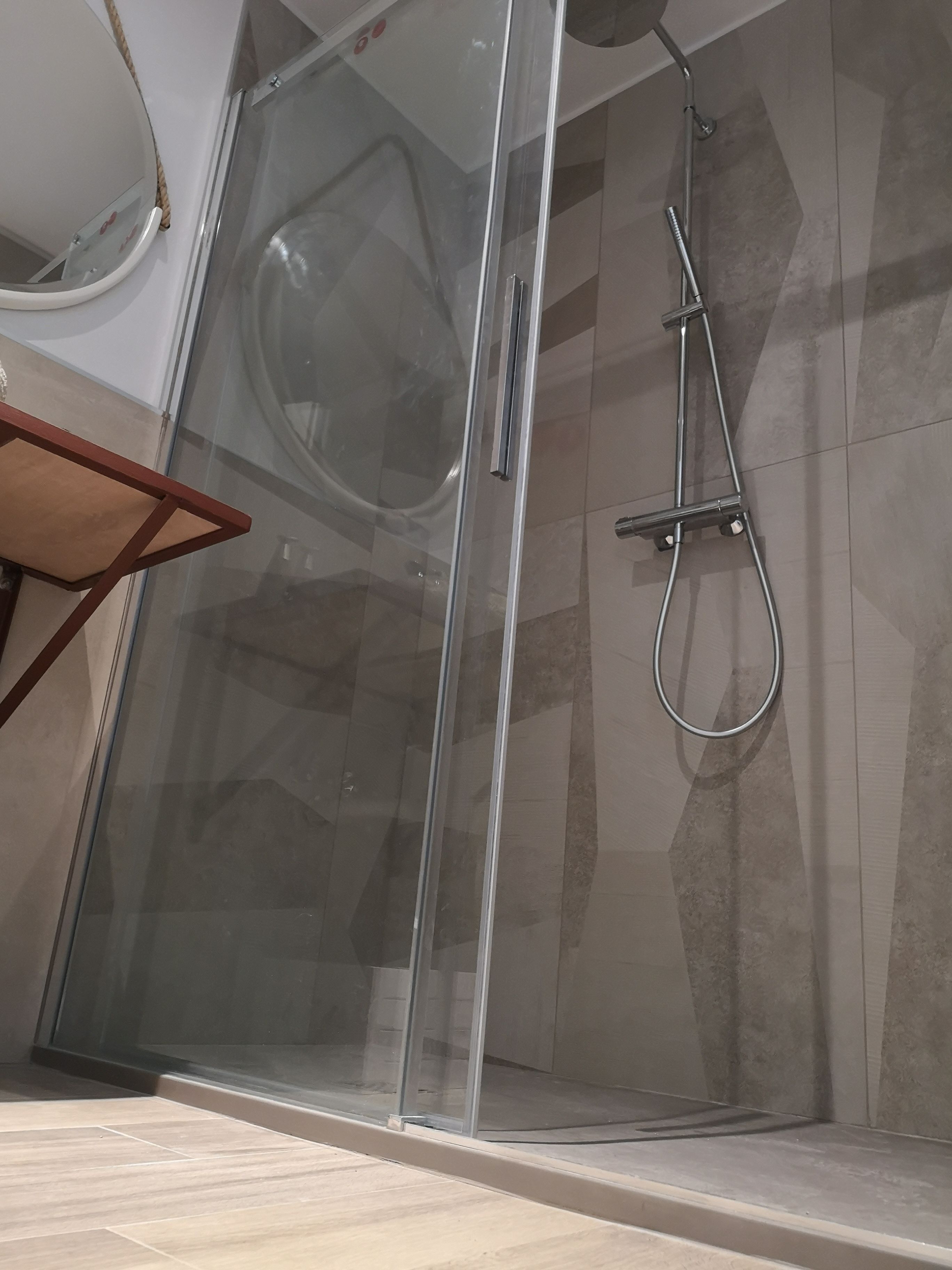 A glass-enclosed shower with a handheld showerhead, a glass door, and a tiled floor.