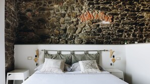A bedroom with a stone wall, a bed with white bedding, two bedside tables, and wall-mounted lamps. - Punto Zero (Vernazza)