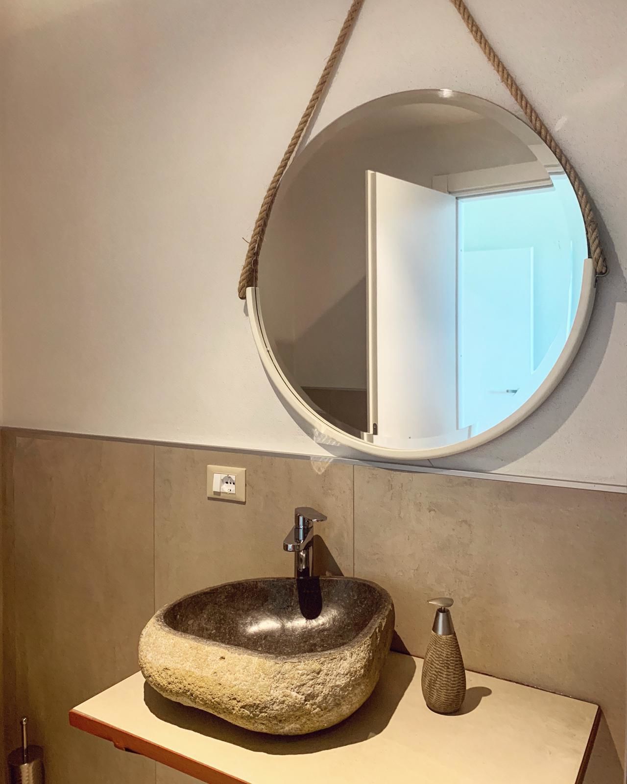 A bathroom with a round mirror, a stone sink, and a small vase.