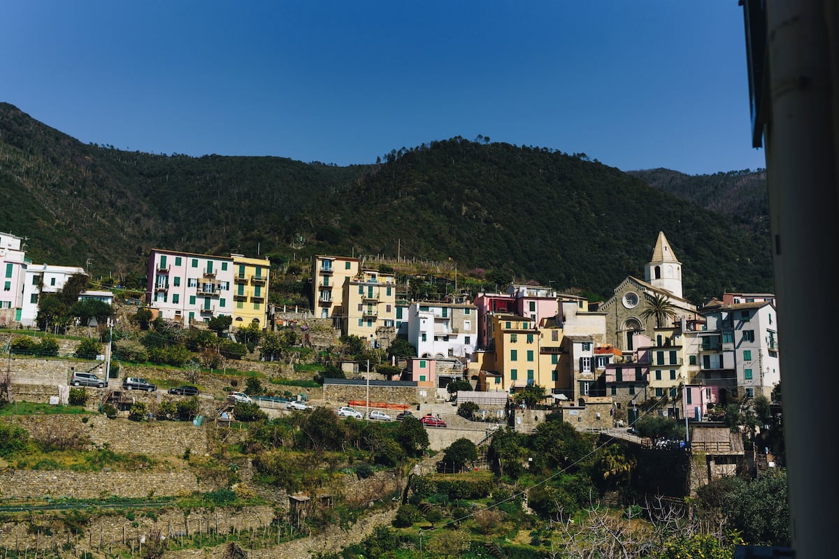 Un pueblo en la ladera con edificios coloridos, una iglesia con un campanario y un puente que conecta las construcciones.