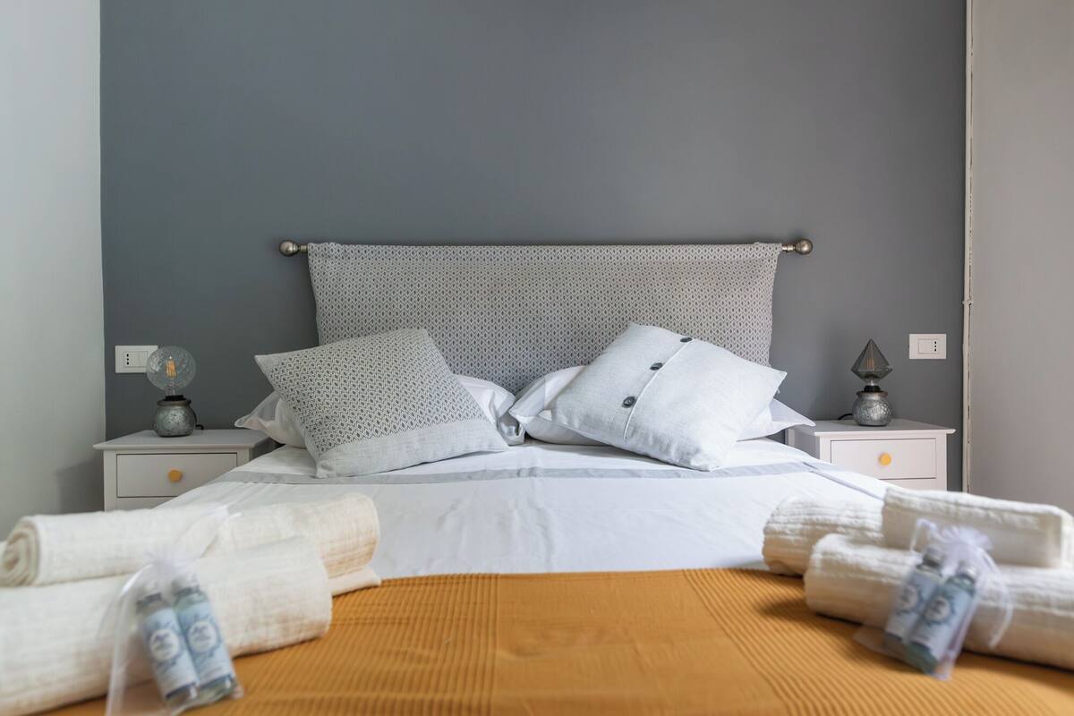 Una cama bien hecha con almohadas, una lámpara de noche y una lámpara de pared.