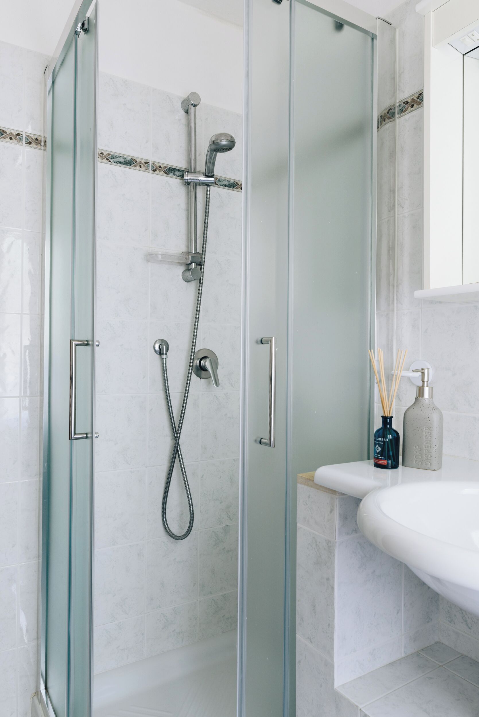 A glass-enclosed shower with a handheld showerhead and a wall-mounted faucet.
