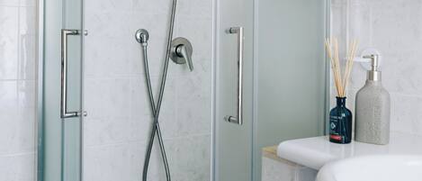 A glass-enclosed shower with a handheld showerhead and a wall-mounted faucet.