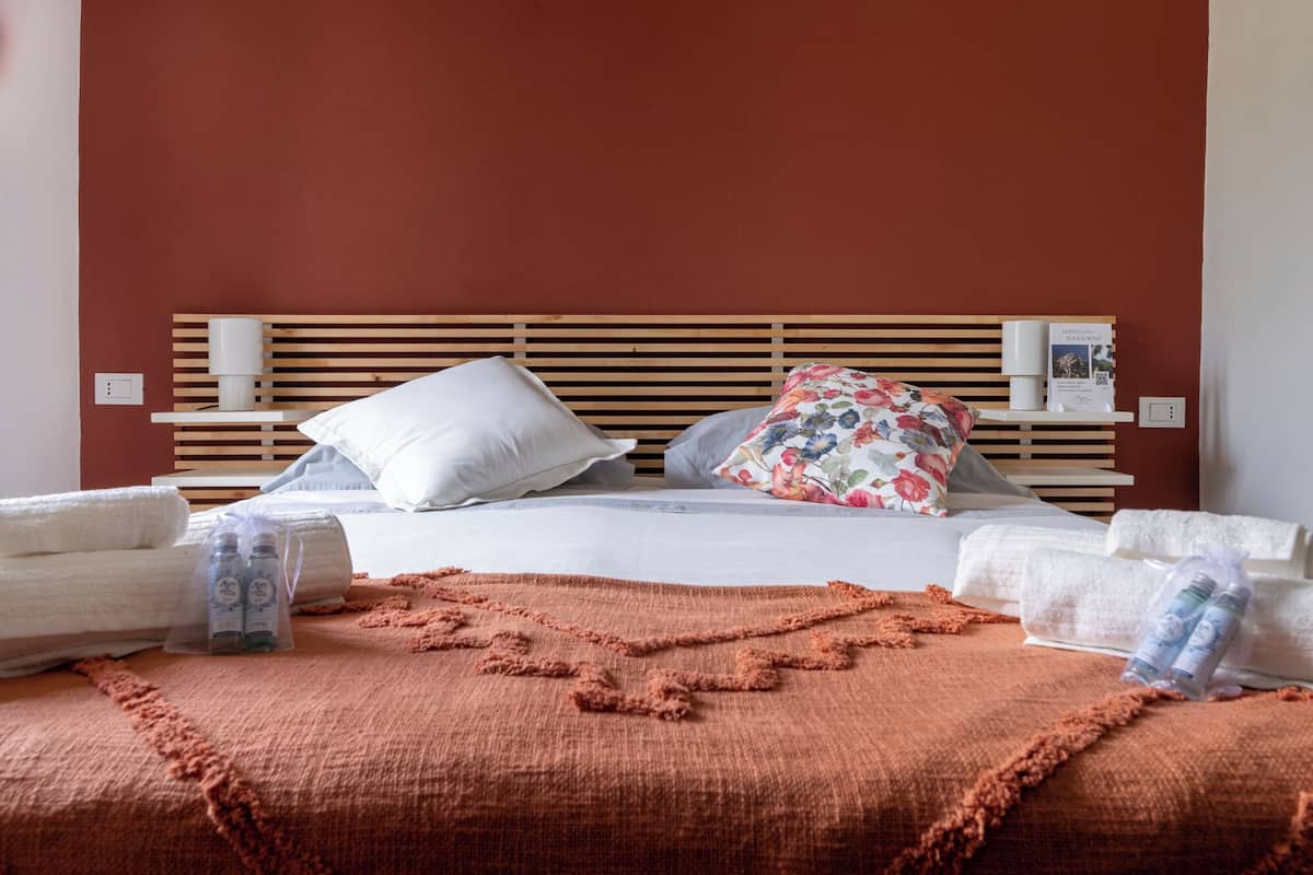Una cama bien hecha con sábanas blancas, cabecera de madera y una manta marrón.